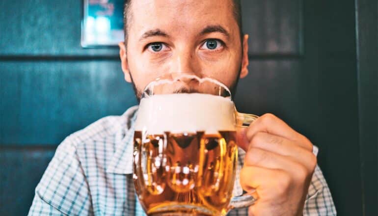 A man looks at the camera as he drinks from a large mug of beer.