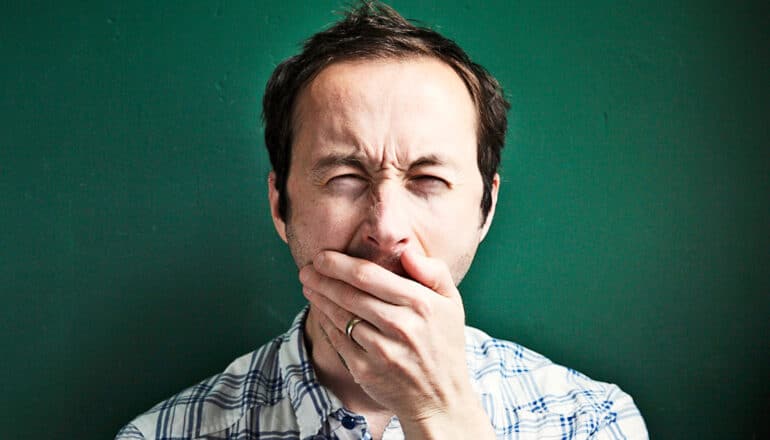 A man closes his eyes and yawns while covering his mouth.