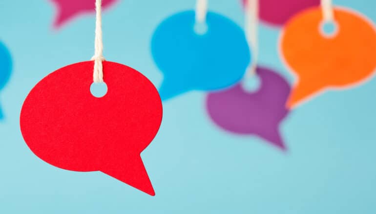 Colorful speech bubbles cut out of paper hang from strings in front of a blue background.