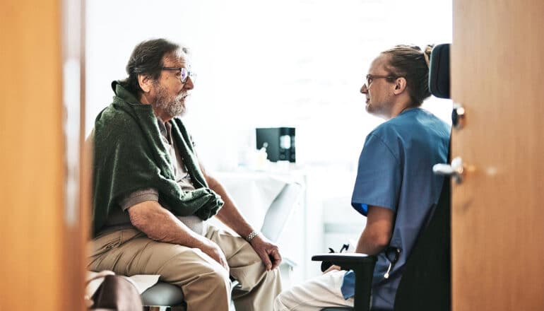 An older man speaks with a doctor in her office.