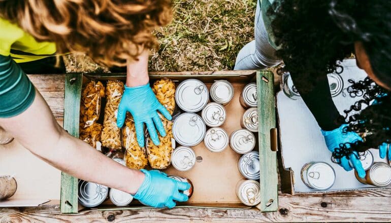 Volunteers wearing blue gloves pack boxes with cans and bags of food.