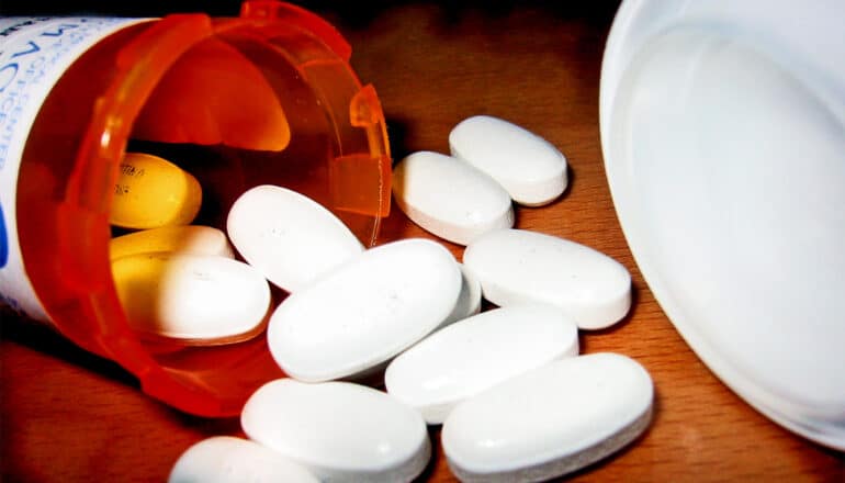 A close up of a pill bottle spilling white pills onto a wooden surface.