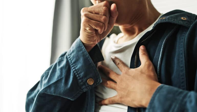 A person covers their mouth and clutches their chest while coughing.