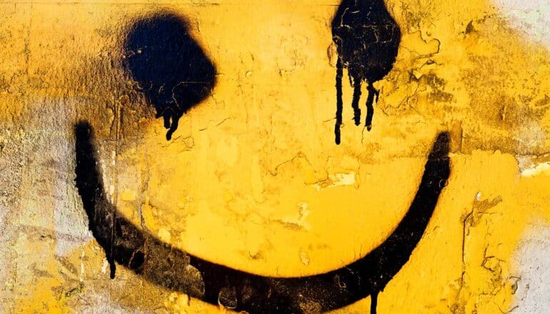 A messy smiley face spray painted in black on yellow paint on a wall.