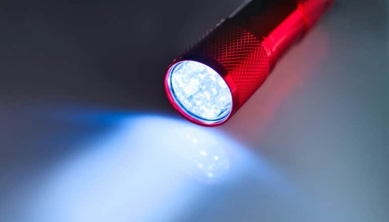 A red flashlight sits on a white surface while shining light.