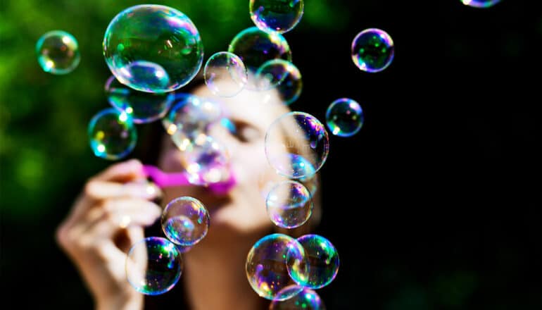 A young girl blows shimmering rainbow-colored bubbles into the air.