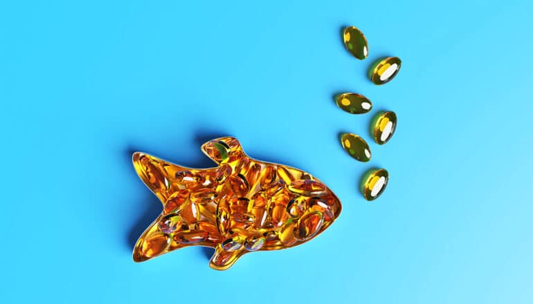 Golden omega 3 capsules arranged in the shape of a fish on a blue background.