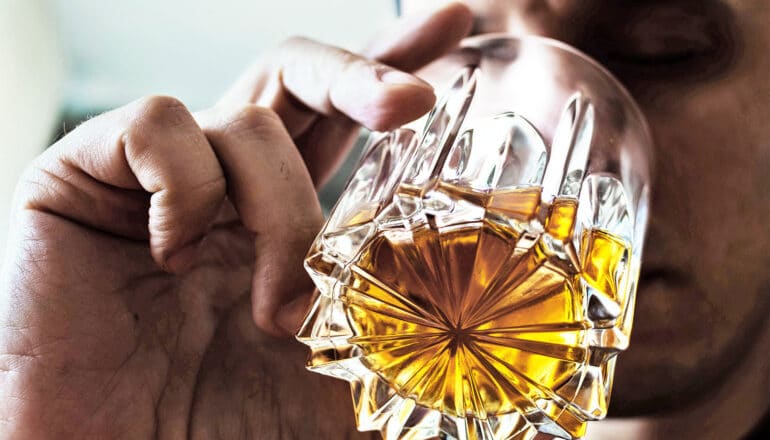 A man holds up a glass of liquor to his lips.