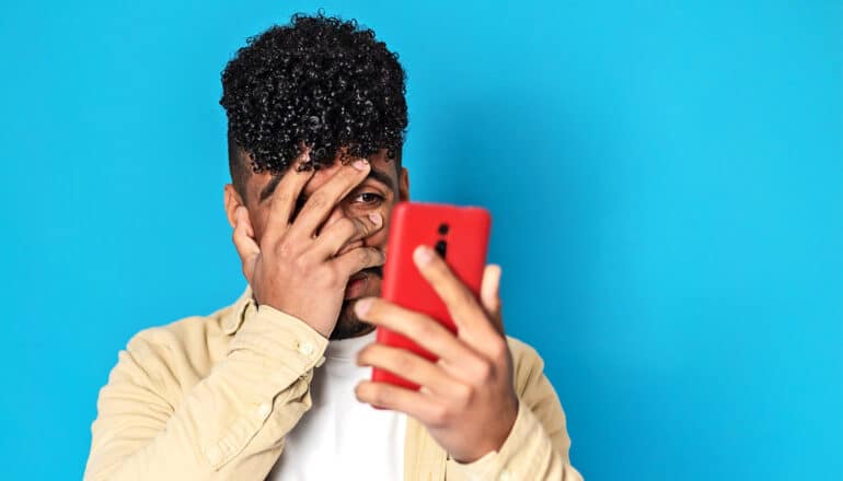 A man covers his face with one hand as he holds his phone with the other.