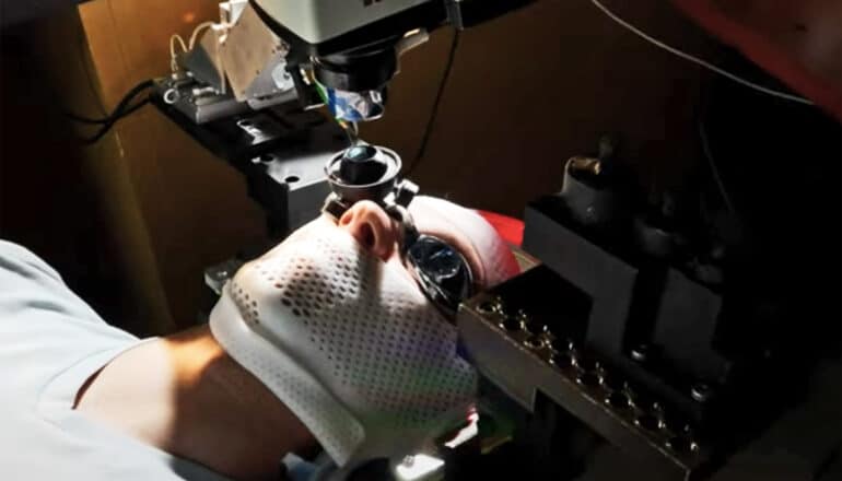 A patient wears a mask over their face and a goggle on one eye as the retina surgery robot hovers over the other eye.