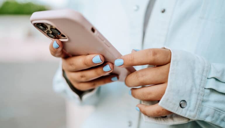 A young woman on with blue nail polish holding her smartphone.