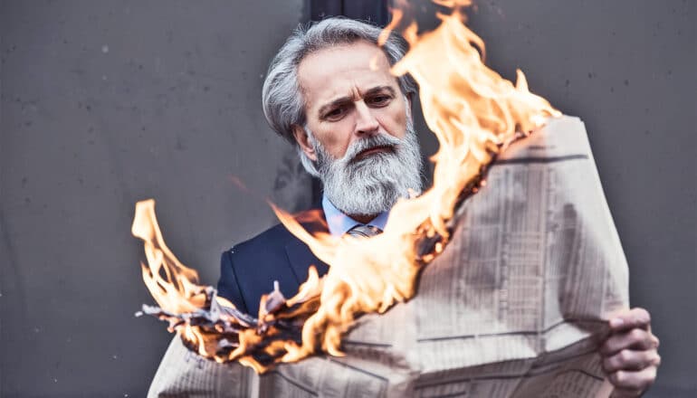 A man reads a newspaper that is on fire.