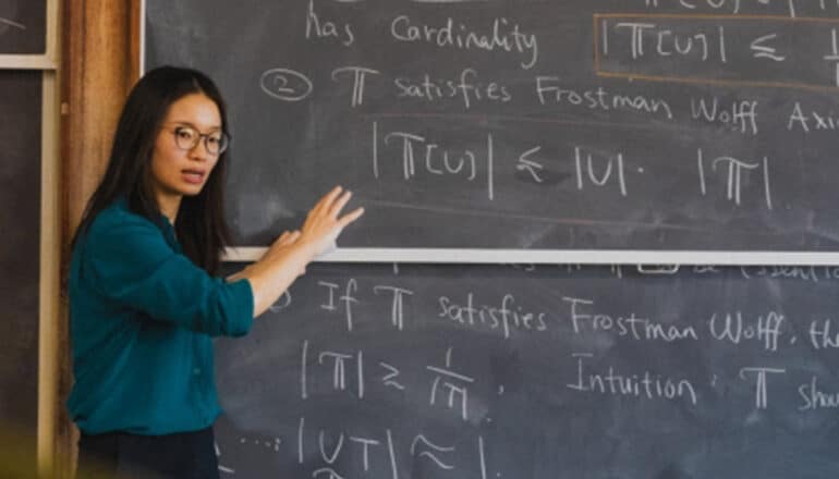 Wang stands in front of a large chalkboard covered in calculations.