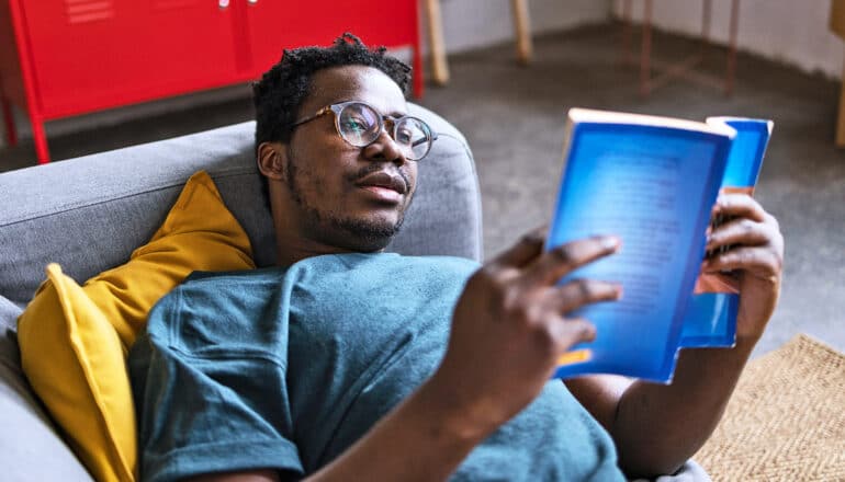 A man lays on his couch reading alone.