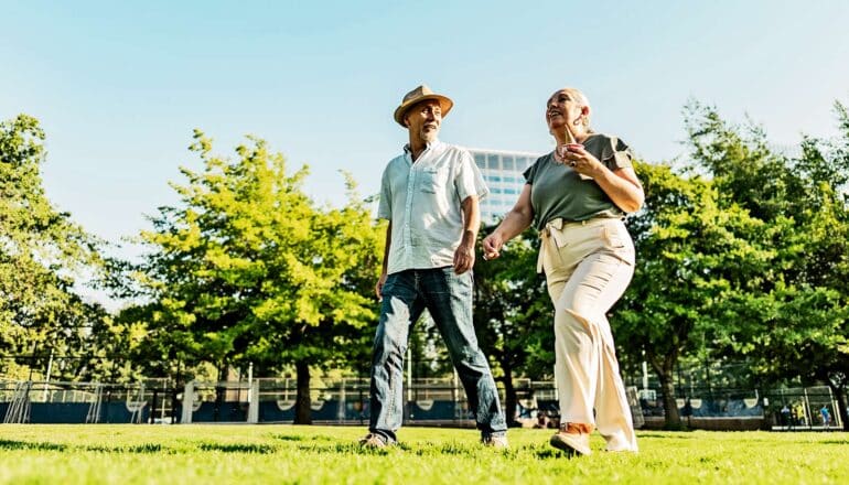 A couple walks on grass through a city park.