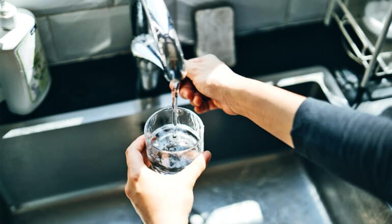 A woman fills a glass of water at a metal sink.